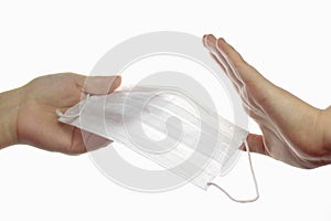 Refusal to wear a protective mask. Hand transmitting a medical mask, the second hand refuses with a gesture. Light background.