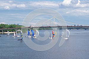 Regatta competition of river sailing yachts boats with white and multicolored sails, reflected sky clouds in water