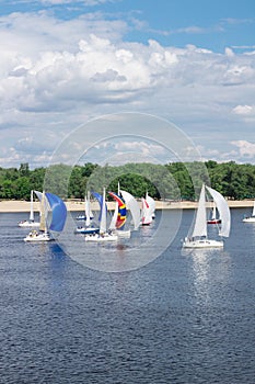 Regatta of lake river sailing yachts boats with white and multicolored sails, reflected sky clouds in water