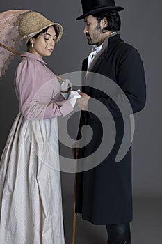 A Regency gentleman wearing a top hat and a lady wearing a bonnet against a grey backdrop