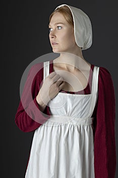 A Regency maid servant wearing a red linen dress with an apron and cap against a studio backdrop
