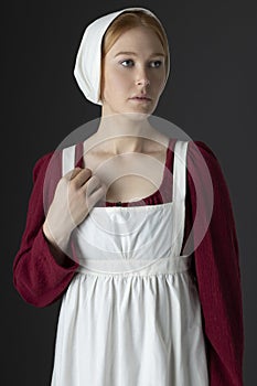 A Regency maid servant wearing a red linen dress with an apron and cap against a studio backdrop