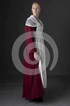 A Regency maid servant wearing a red linen dress with an apron and a lace modesty shawl against a studio backdrop