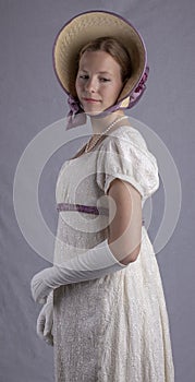 Regency woman in cream dress and bonnet on studio backdrop