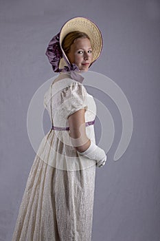 Regency woman in cream dress and bonnet on studio backdrop