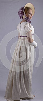 Regency woman in cream dress and bonnet on studio backdrop