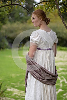 Regency woman in cream dress and bonnet walks in a summer garden