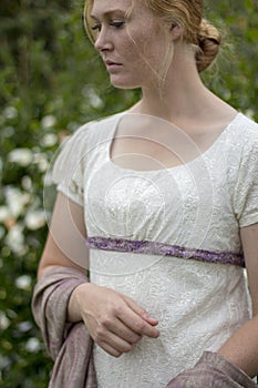 Regency woman in cream dress and bonnet walks in a summer garden