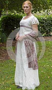 Regency woman in cream dress walks alone in a summer garden