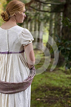 Regency woman in cream dress walks alone in a summer garden