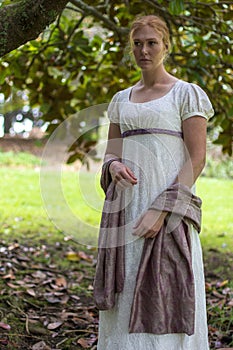 Regency woman in cream dress walks alone in a summer garden