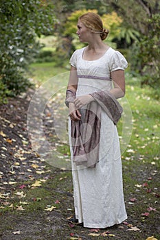 Regency woman in cream dress walks alone in a summer garden