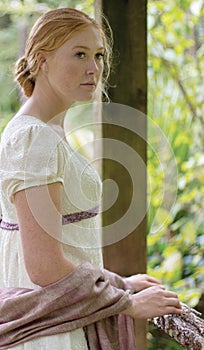 Regency woman in cream dress walks alone in a summer garden