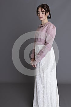 A Regency woman wearing a cream embroidered dress and a pink linen short spencer