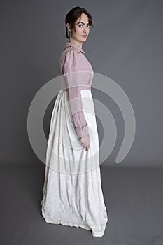 A Regency woman wearing a cream embroidered dress and a pink linen short spencer