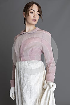 A Regency woman wearing a cream embroidered dress and a pink linen short spencer