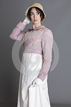 A Regency woman wearing a cream embroidered dress and a pink linen short spencer