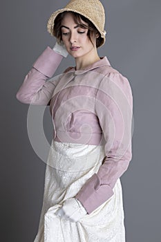 A Regency woman wearing a cream embroidered dress and a pink linen short spencer