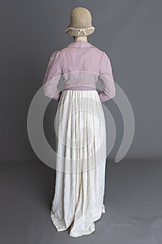 A Regency woman wearing a cream embroidered dress and a pink linen short spencer