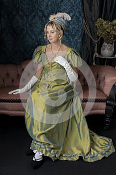 A Regency woman wearing a green shot silk dress and sitting on a pink sofa
