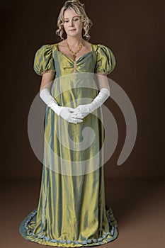 A Regency woman wearing a green shot silk dress and standing against a studio backdrop
