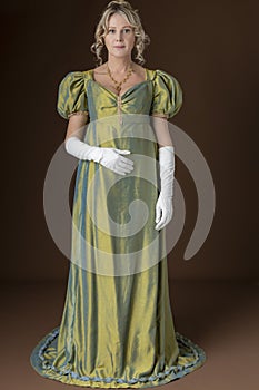 A Regency woman wearing a green shot silk dress and standing against a studio backdrop