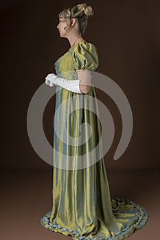 A Regency woman wearing a green shot silk dress and standing against a studio backdrop