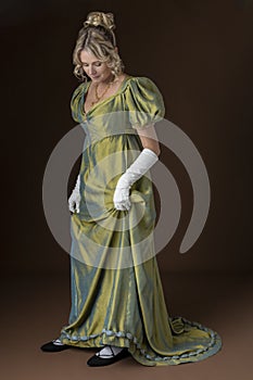 A Regency woman wearing a green shot silk dress and standing against a studio backdrop