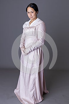 A Regency woman wearing a printed cotton dress and lace modesty shawl against a grey backdrop