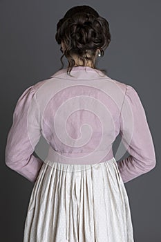 A Regency woman wearing a printed cotton dress and a pink linen short spencer and a pink linen short spencer