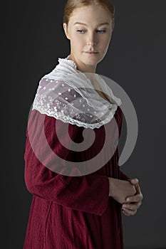 A Regency woman wearing a  red linen dress with  a lace modesty shawl against a studio backdrop