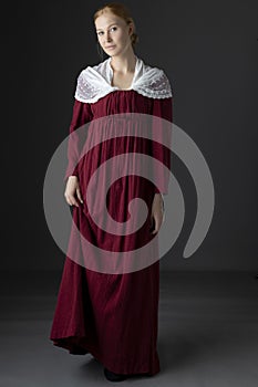 A Regency woman wearing a  red linen dress with  a lace modesty shawl against a studio backdrop