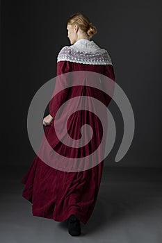 A Regency woman wearing a  red linen dress with  a lace modesty shawl against a studio backdrop