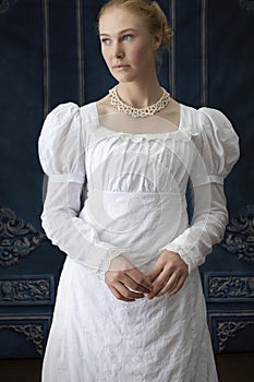 A Regency woman wearing a white cotton muslin dress and standing in a room