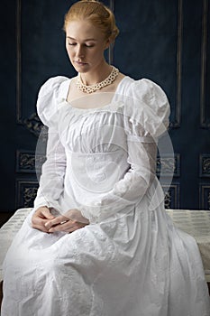 A Regency woman wearing a white cotton muslin dress and standing in a room