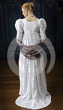 A Regency woman wearing a white cotton muslin dress and standing in a room