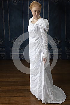 A Regency woman wearing a white cotton muslin dress and standing in a room