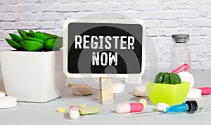 REGISTER NOW written on a paper with office tools and keyboard on the grey background