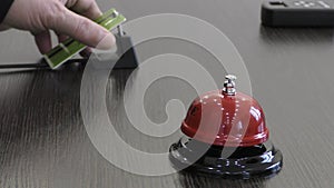 Registration. A man`s hand rings a bell at the front desk.