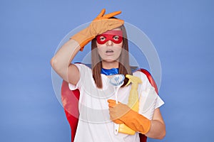 Regretful brown haired woman wearing superhero costume mask and protective rubber gloves posing isolated over blue background