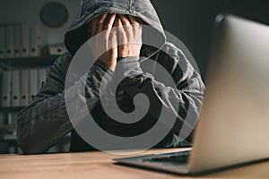 Regretful computer hacker covering face with hands in front of laptop