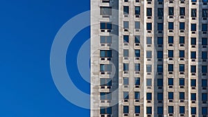 Regular pattern made of rectangular windows on block of flats / offices building. Clear sky place for text on left side