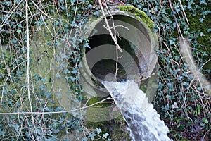 Regulated stream or brook coming from underground out of a large pipe in a small waterfall