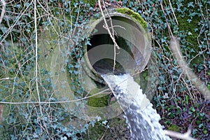 Regulated stream or brook coming from underground out of a large pipe in a small waterfall from a vertical wall.
