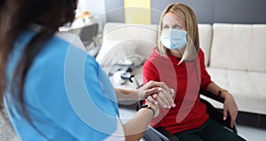 Rehabilitation doctor in protective medical mask communicates with a disabled woman in wheelchair