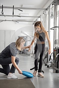 Rehabilitation specialist helping little girl to do exercises at gym