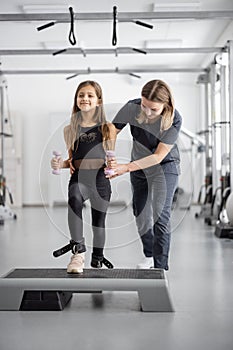 Rehabilitation specialist helping little girl to do exercises at gym