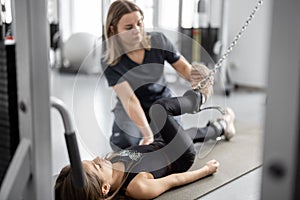 Rehabilitation specialist helping little girl to do exercises on simulators at gym