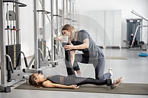 Rehabilitation specialist helping little girl to do exercises on simulators at gym