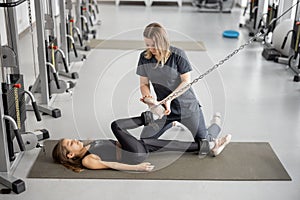 Rehabilitation specialist helping little girl to do exercises on simulators at gym